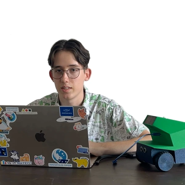 Юноша работает за ноутбуком, рядом стоит робот Pixelbot, подключённый кабелем
